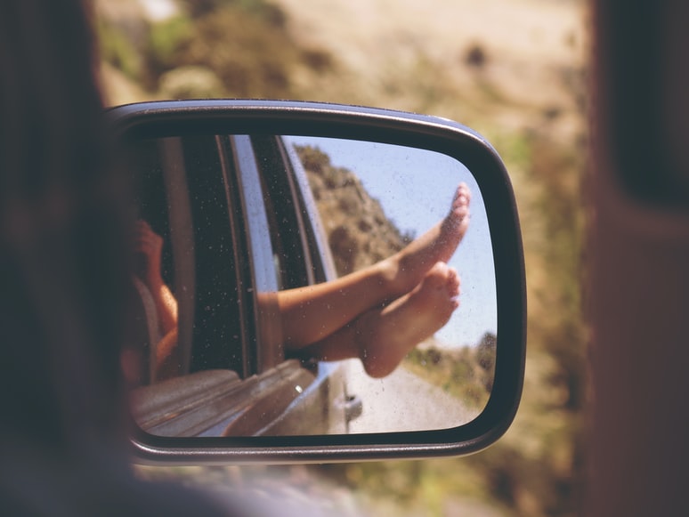 Feet sticking out of vehicle window, reflected on car side mirror