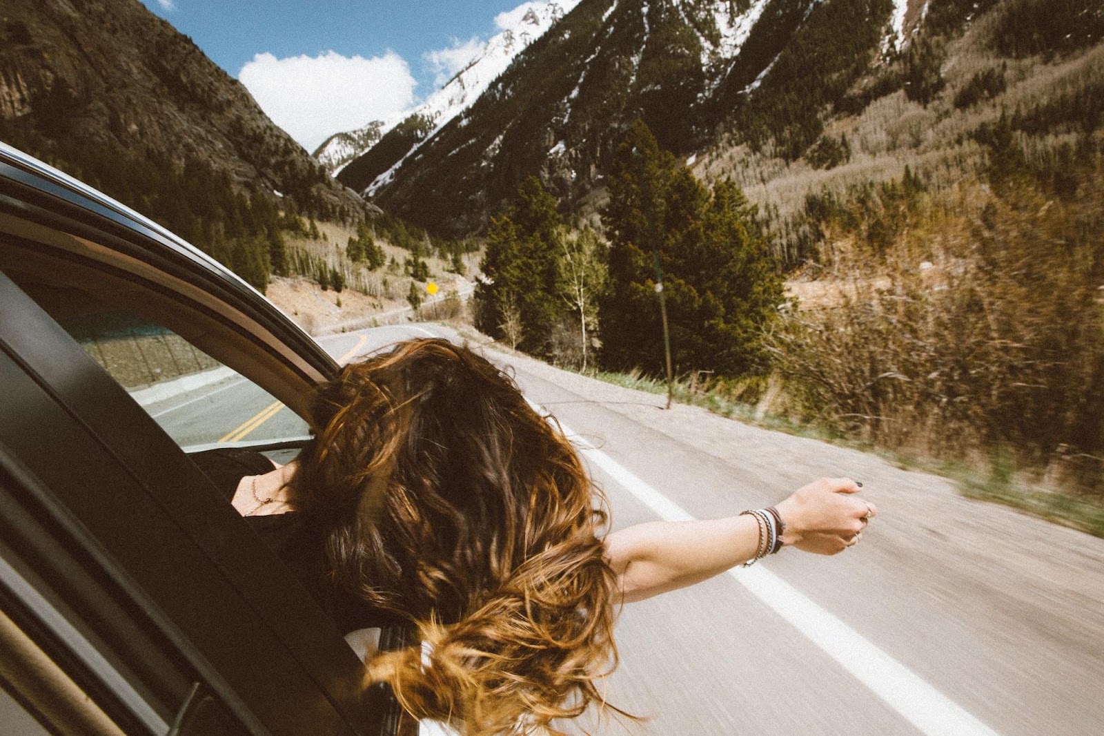 Woman leaning head out passenger side vehicle window, arm stretched out